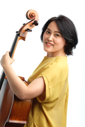 Smiling woman in a yellow top holding a cello posing for a portrait